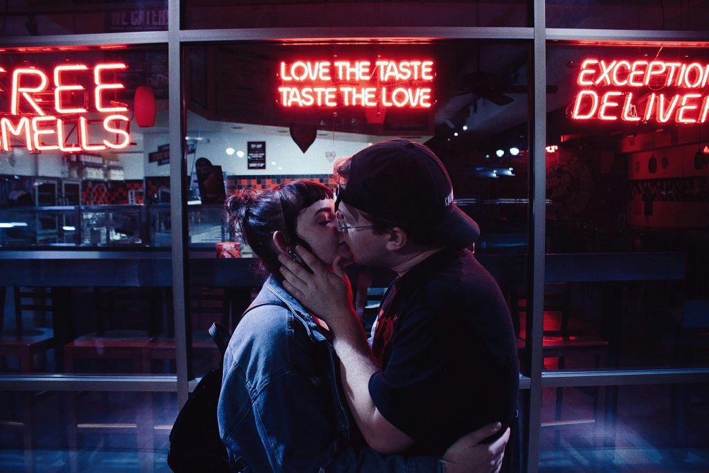 A couple shares a romantic kiss at night under vibrant neon signs in Chattanooga.