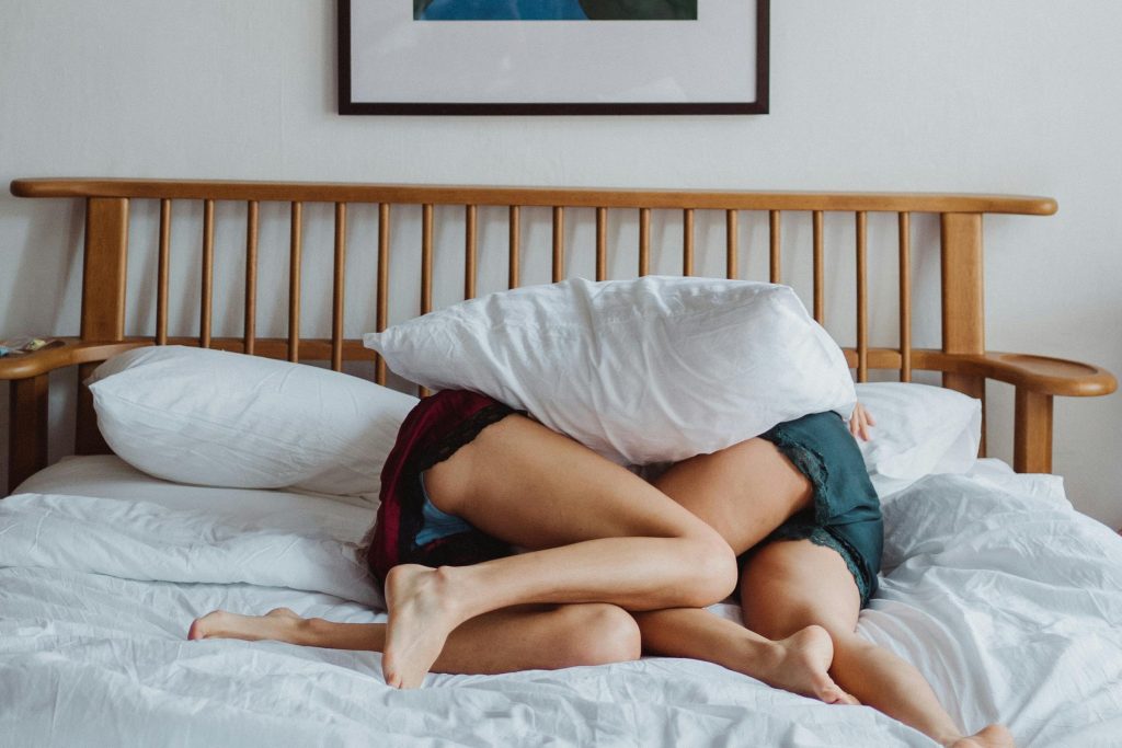 A cozy moment in bed with a couple embracing under pillows.